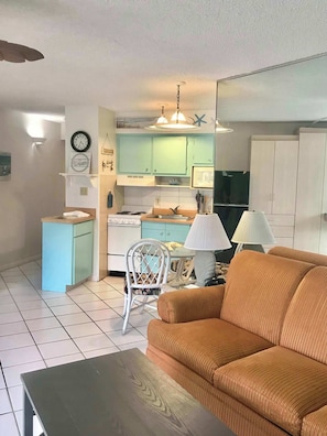 Un espacio habitable compacto con sofá, mesa de comedor, cocina con estufa y televisor.