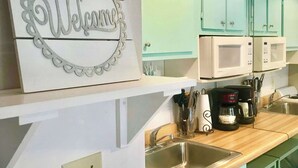 A kitchen with teal cabinets, a clock, a welcome sign, and a coffee maker.