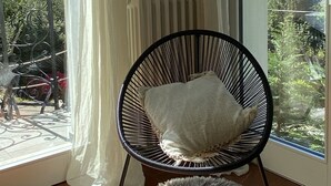 Huone, josta avautuu näkymä vehreään maisemaan, pehmustettu tuoli ja pieni, pehmeä jakkara.