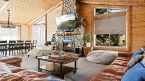L’intérieur chaleureux d’un chalet en rondins, avec une cheminée en pierre, des meubles en cuir et de grandes fenêtres donnant sur la forêt.