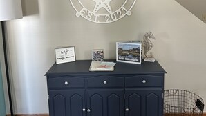 A wall with a circular sign reading "ONAWHILE EST 2021" and a dark blue cabinet with various items on top. - On a Whim, a family retreat! (Chincoteague)