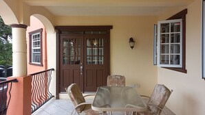Un portico coperto con tavolo e sedie, una porta marrone e una finestra con un cartello.