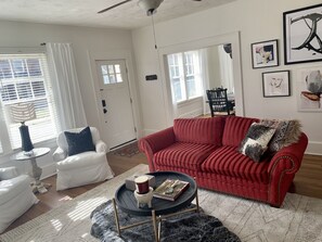 Un salón con un sofá rojo, un sillón blanco y una mesa de centro redonda con libros y una vela.
