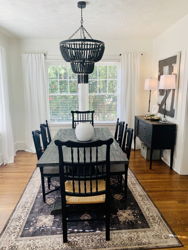 Comedor con una mesa de madera oscura, sillas negras, un jarrón blanco y una araña negra.