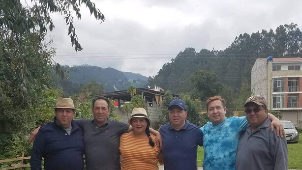 Un grup de persones de peu a l'exterior, amb un paisatge amb muntanyes al fons.
