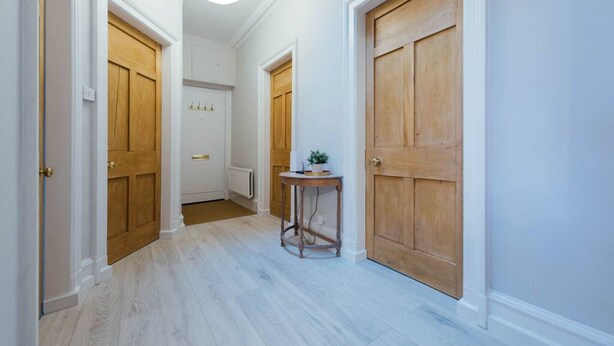A hallway with wooden doors, a small round table with a plant, and a white ceiling light. - The Riverside Apartment (free parking) (Stirling)