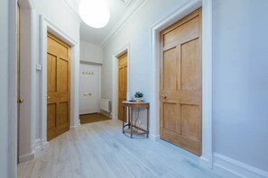 A hallway with wooden doors, a small round table with a plant, and a white ceiling light. - The Riverside Apartment (free parking) (Stirling)