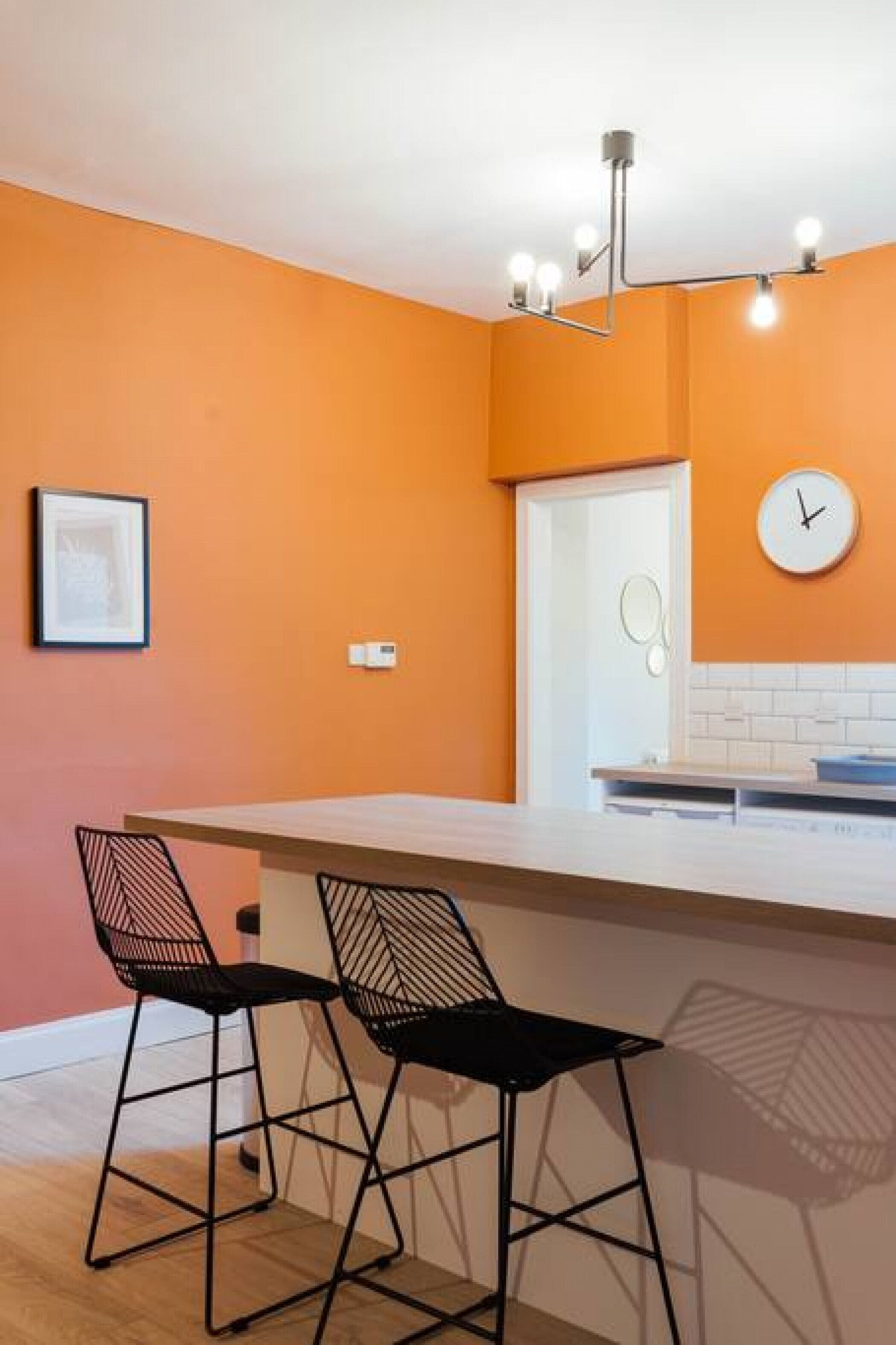 Eine moderne Küche mit zwei schwarzen Stühlen, einer weißen Arbeitsplatte und einer orangefarbenen Wand.