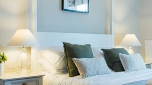 A modern bedroom with a white bed, two bedside tables with lamps, a framed picture on the wall, and a patterned rug. - The Riverside Apartment (free parking) (Stirling)