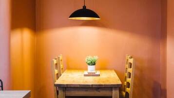 A dining area with a wooden table and chairs, a hanging pendant light, and a small potted plant on the table.