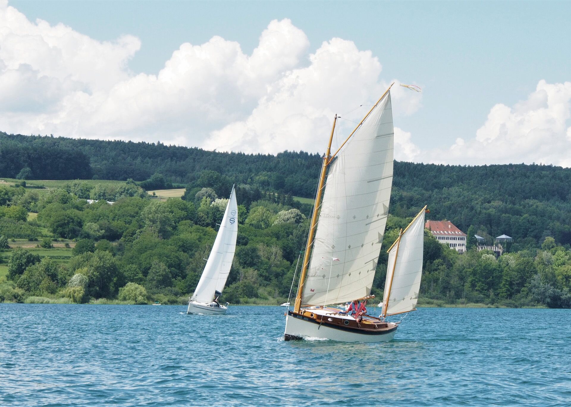 A sailboat on a lake with a forested hillside in the background.