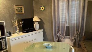Un espace de vie compact comprenant une table à manger, deux chaises, un téléviseur, une lampe et un petit objet décoratif posé sur une étagère.