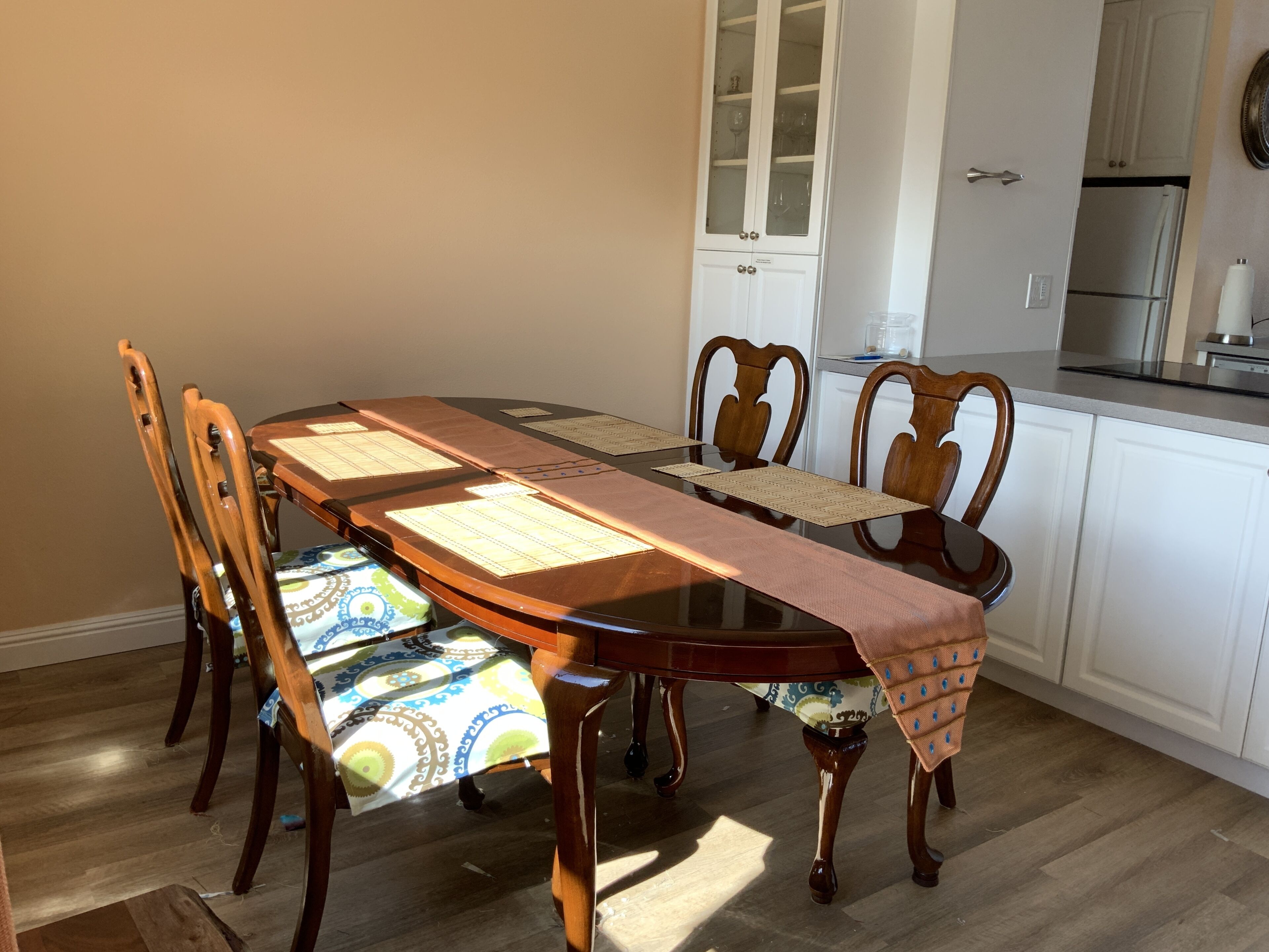 A dining table with chairs, a kitchen area, and a cabinet with glass doors.
