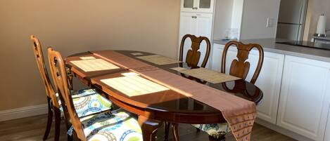A dining table with chairs, a kitchen area, and a cabinet with glass doors.