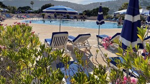 Zona de piscina amb gandules i ombrel·les, cel clar i vista llunyana d'un paisatge amb turons.