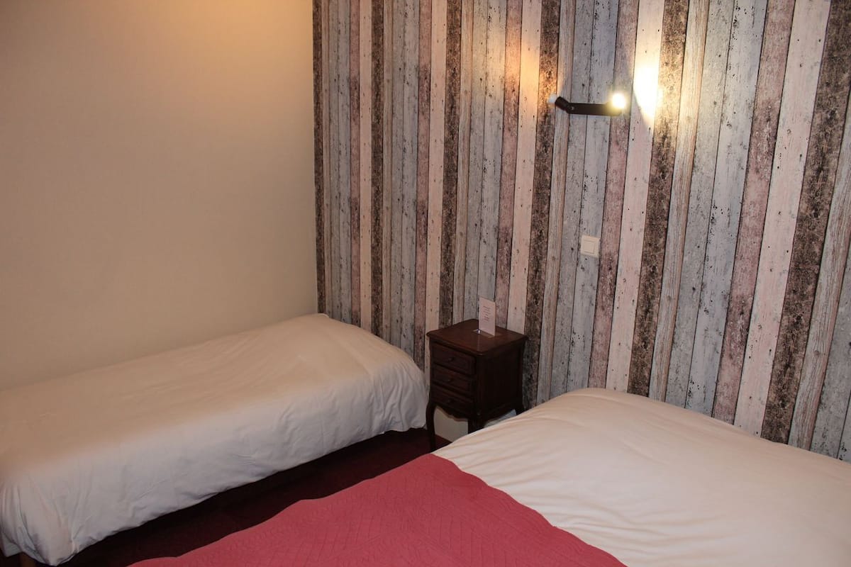 A room with two single beds, a wooden wall with vertical stripes, a small wooden nightstand, and a wall-mounted light fixture.