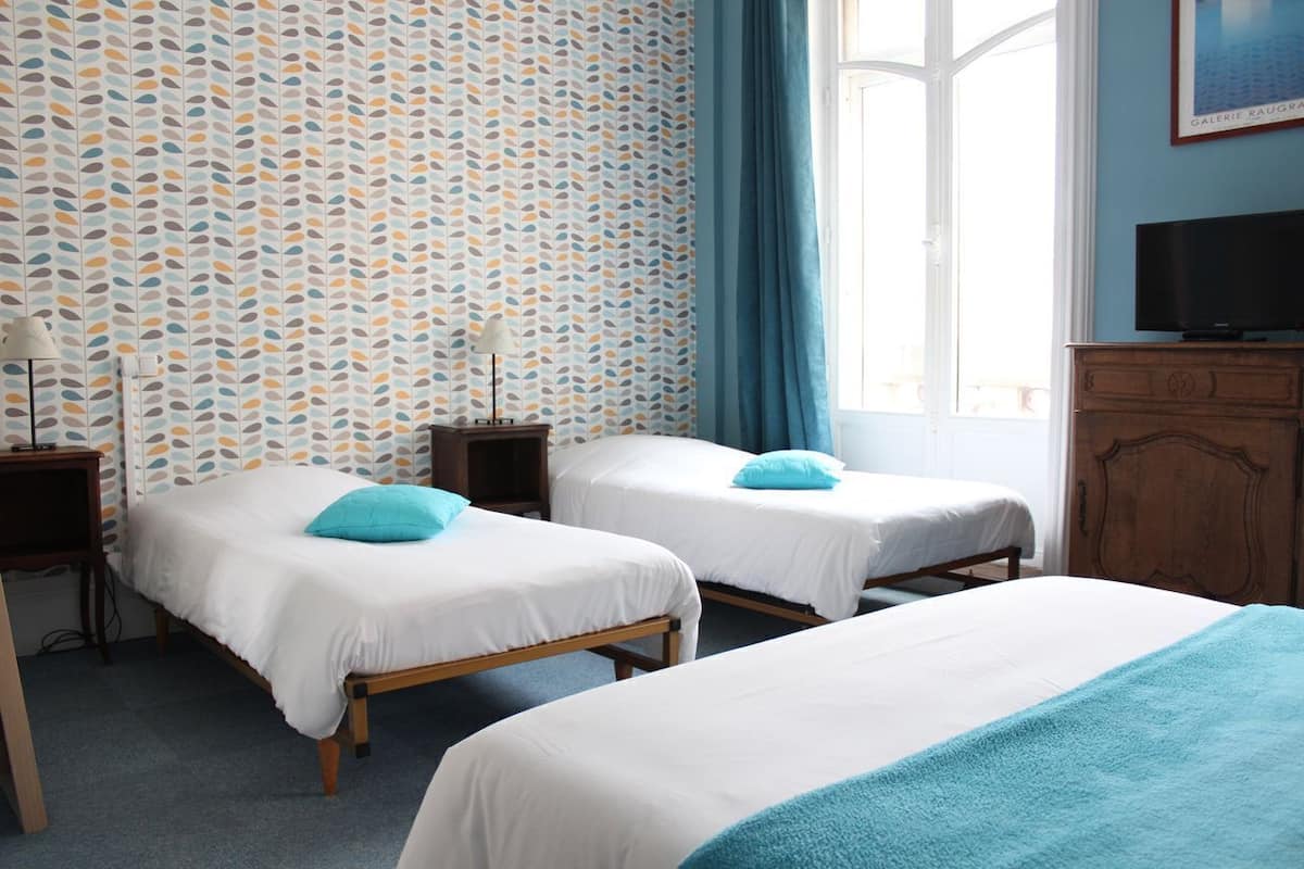 A hotel room with two beds, a TV, a wooden cabinet, and a patterned wallpaper.