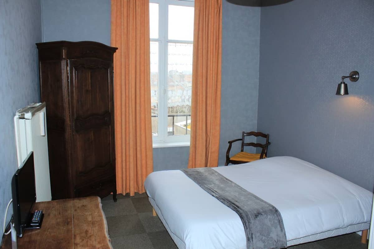 A bedroom with a bed, a wooden wardrobe, a chair, a radiator, and a window with curtains.