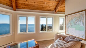 A room with large windows overlooking the sea, a wooden ceiling, and a map on the wall. - Sunrise Catcher with a Panoramic View!  (Harpswell)