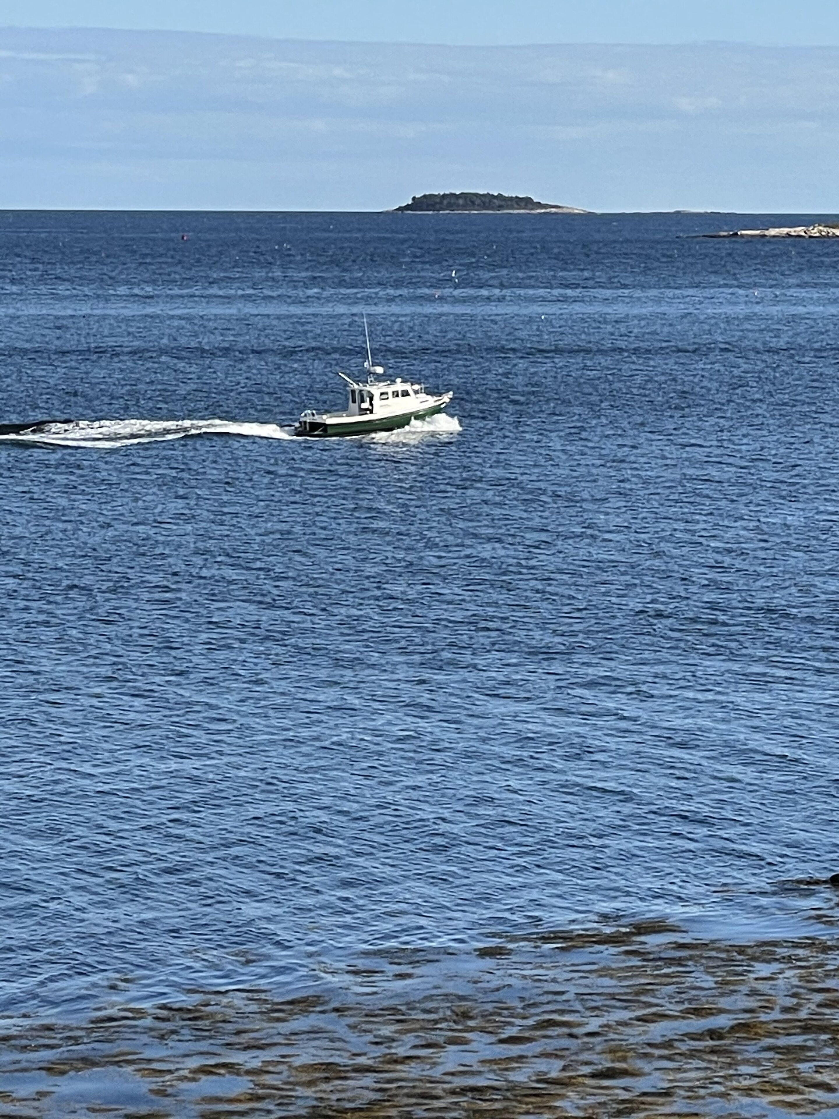 A boat moving across a calm sea with a distant island.
