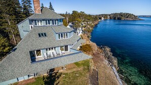 A large house with a sloped roof, a covered patio with outdoor furniture, and a view of a lake. - Sunrise Catcher with a Panoramic View!  (Harpswell)