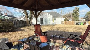 Un patio al aire libre con mobiliario de mimbre y un tapiz estampado bajo un toldo de madera.