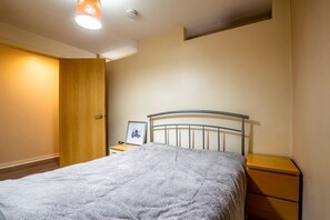 A bedroom with a bed, a nightstand, a wooden wardrobe, and a framed picture on the nightstand.