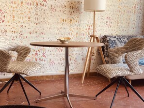 Cozy interior space with a round table and two chairs, surrounded by a floral wallpaper and terracotta tiles.