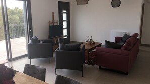 Ein Wohnzimmer mit einer Couch, Sesseln, einem Couchtisch und einem Fernseher auf einem Schrank.