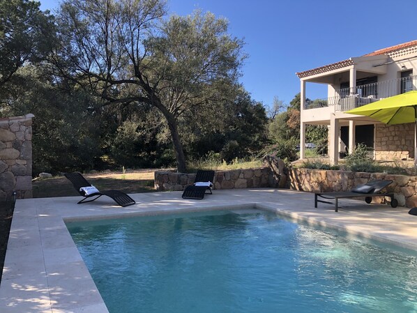 A pool area with lounge chairs and a stone wall. - Detached, air-conditioned villa. Swimming pool. A garden with trees. Near the beaches (San-Gavino-Di-Carbini)