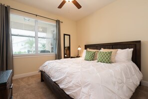 A bedroom with a bed, a nightstand, a lamp, a window with curtains, and a ceiling fan.