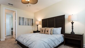 A bedroom with a large bed, two bedside tables with lamps, a wooden headboard, a wall-mounted artwork, and a door leading to another room. - Disney Dreams Luxury Home with Private Water Park (Kissimmee)