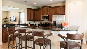 A modern kitchen with dark wood cabinets, stainless steel appliances, and a central island with bar stools. - Disney Dreams Luxury Home with Private Water Park (Kissimmee)