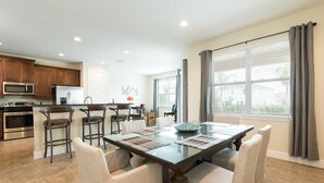 A modern kitchen with stainless steel appliances, a dining area with a glass table and cushioned chairs, and large windows with curtains. - Disney Dreams Luxury Home with Private Water Park (Kissimmee)