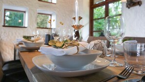 Een eettafel gedekt met witte borden, kommen en een wijnglas, met een kaars en decoratieve bladeren in het midden.