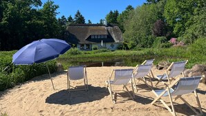 Een strand met ligbedden en een huis met rieten dak op de achtergrond.