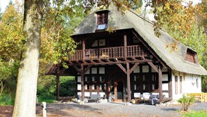 Een rustiek houten gebouw met rieten dak, een balkon en een veranda met zitplaatsen.