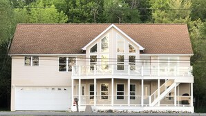 A two-story house with a front porch, a garage, and a staircase leading to a second-floor balcony. - Waterfront Lake House - Portage Lake - 4 Beds, 3 Baths, Private Dock, Kayaks (Onekama)