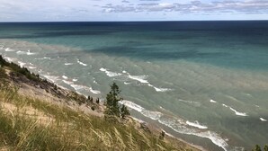 A coastal landscape with clear waters, a sandy beach, and grassy cliffs. - Waterfront Lake House - Portage Lake - 4 Beds, 3 Baths, Private Dock, Kayaks (Onekama)