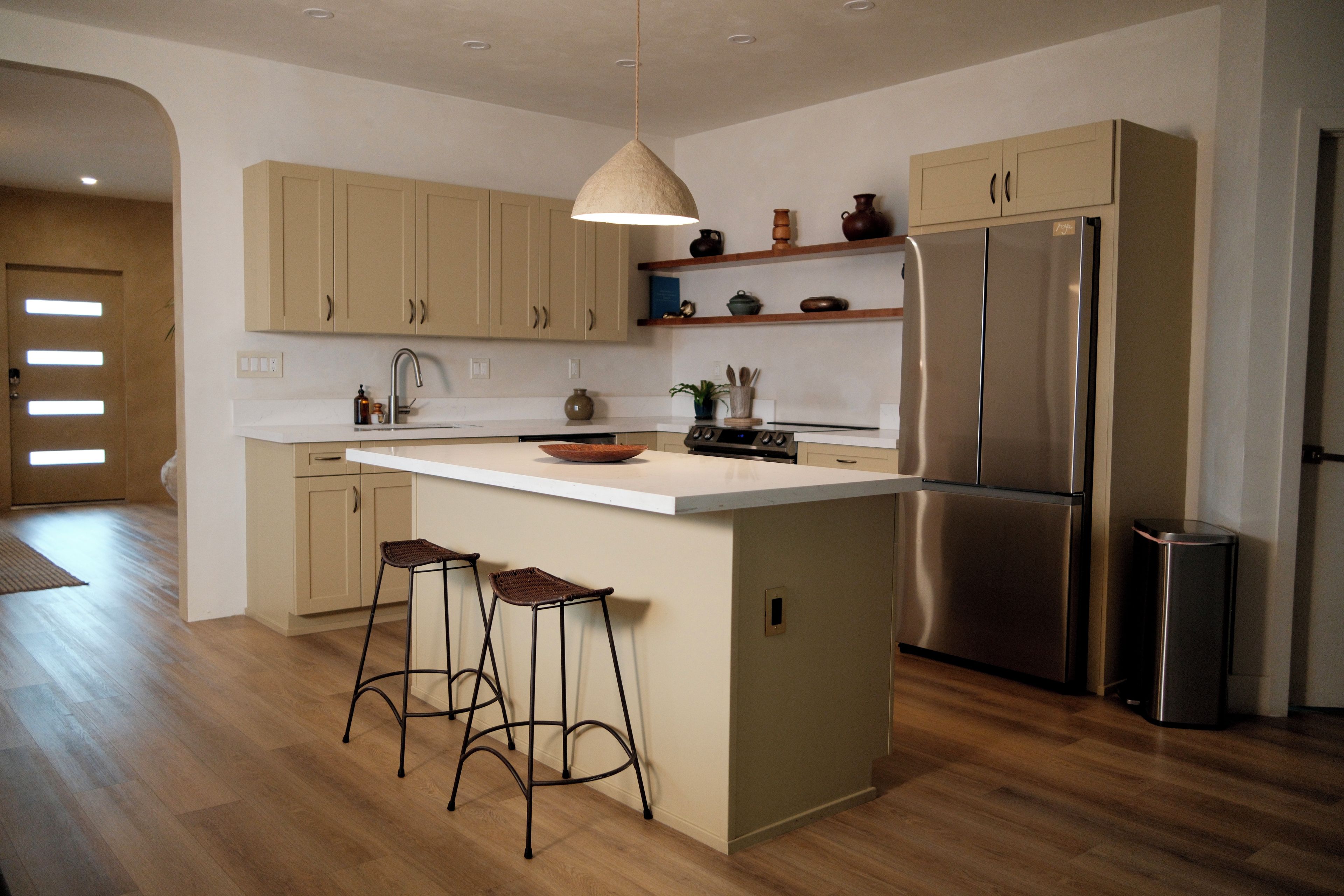 A modern kitchen with a central island, bar stools, a stainless steel refrigerator, and wooden cabinets.