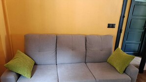 A grey sofa with two green cushions against a yellow wall.