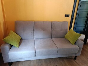 A grey sofa with two green cushions against a yellow wall.