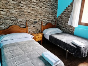 Quarto com duas camas, parede de pedra, mesa de cabeceira de madeira e janela com cortinas.