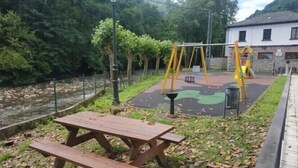 A picnic table and playground equipment near a river, with a building in the background.