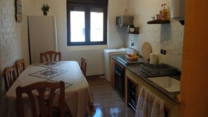 A compact kitchen with a dining area, featuring a window, a clock, and basic appliances.
