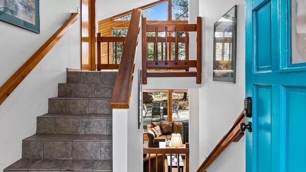 Un escalier avec des rampes en bois, une porte bleue et une vue sur un espace extérieur aménagé avec des sièges.