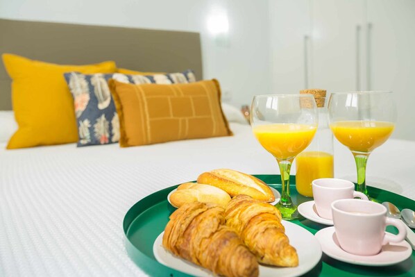 Ein Frühstücksbrett mit Croissants, Saft und Kaffeetassen auf einem Bett mit Kissen und einem weißen Kopfteil.
