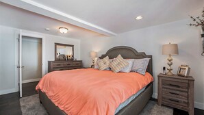 A bedroom with a large bed, two bedside tables with lamps, a dresser, and a mirror. - Colorado Mountain Getaway Retreat (Idaho Springs)