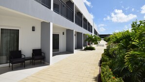 Un hotel moderno con un área de estar al aire libre techada, un sendero empedrado y abundante vegetación.