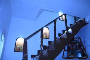 A staircase with a wooden handrail and a glass railing, leading to a landing with a bookshelf and a framed picture.